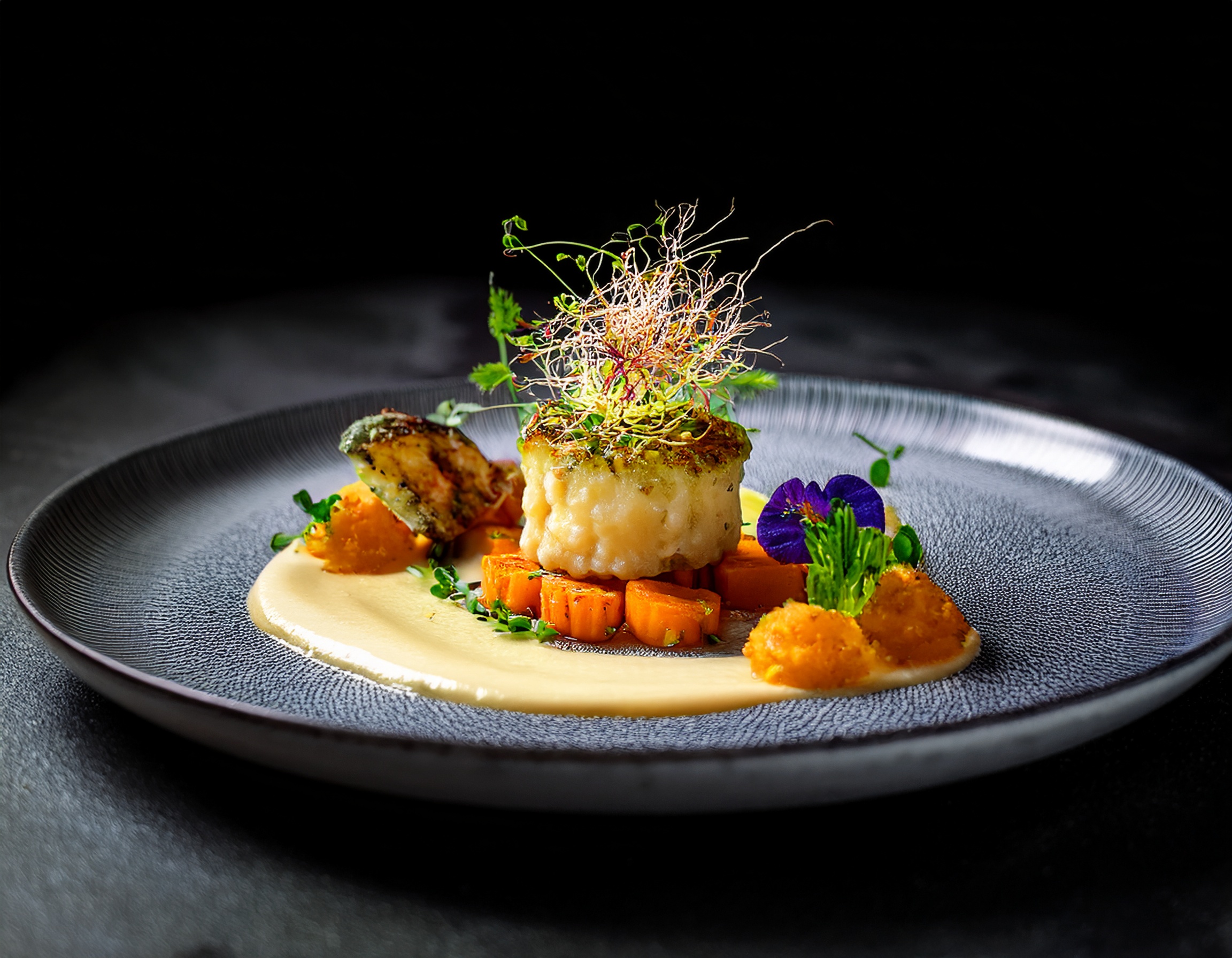 Ein veganes Haute-Cuisine-Gericht auf Michelin-Sterne-Niveau, bestehend aus geröstetem Blumenkohlsteak, Trüffel-Kartoffelpüree, karamellisierten Karotten und einer feinen Kräuteremulsion.