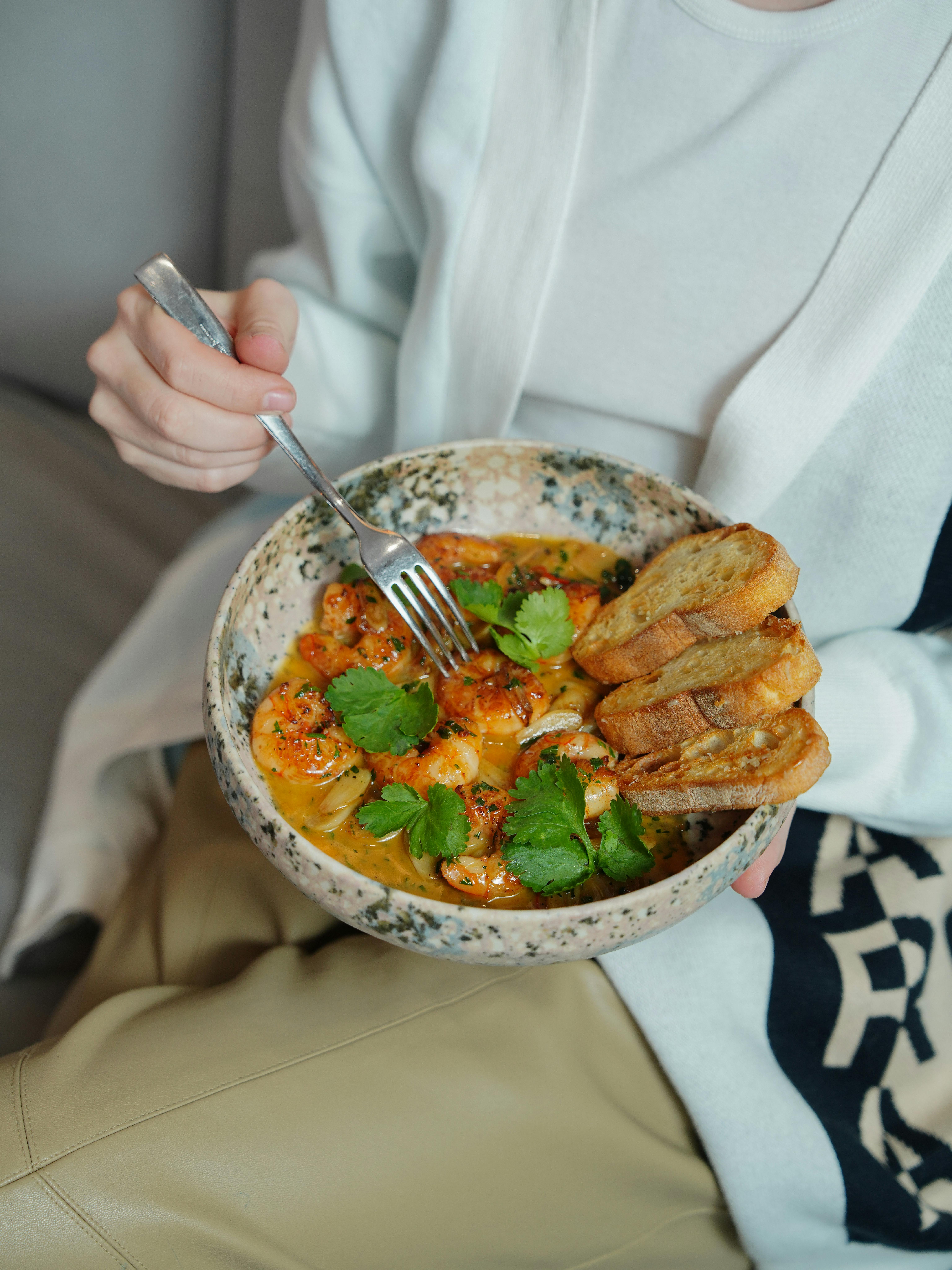 Schüssel mit Garnelen-Curry und Petersilie, dabei liegen drei getoastete Scheiben Baguette.
